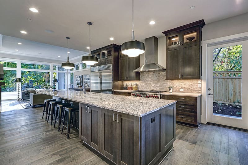 Oversized Kitchen Island In A Modern Kitchen With Bar Stools Granite Countertops Huge Refrigerator And Beige Backsplash